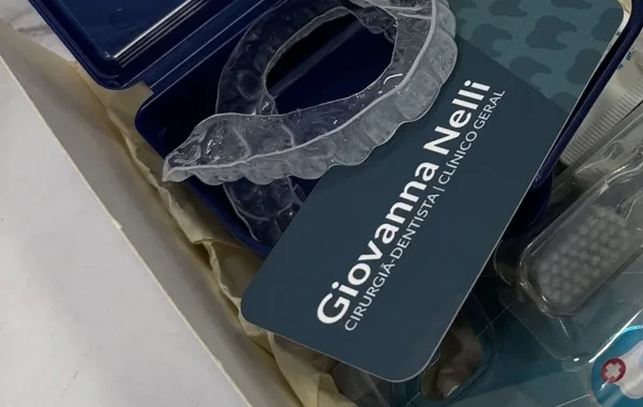 Kit em caixa de papel com estojo azul, aparelho transparente, escova e o cartão Giovanna Nelli, cirurgiã-dentista